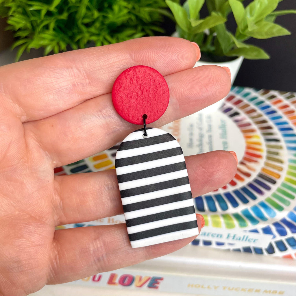 Hand holding a black & white striped earring with a red top