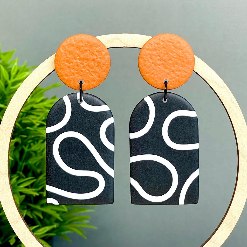 Pair of earrings with orange tops and black and white squiggle patterned bottoms