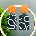 Pair of earrings with orange tops and black and white squiggle patterned bottoms