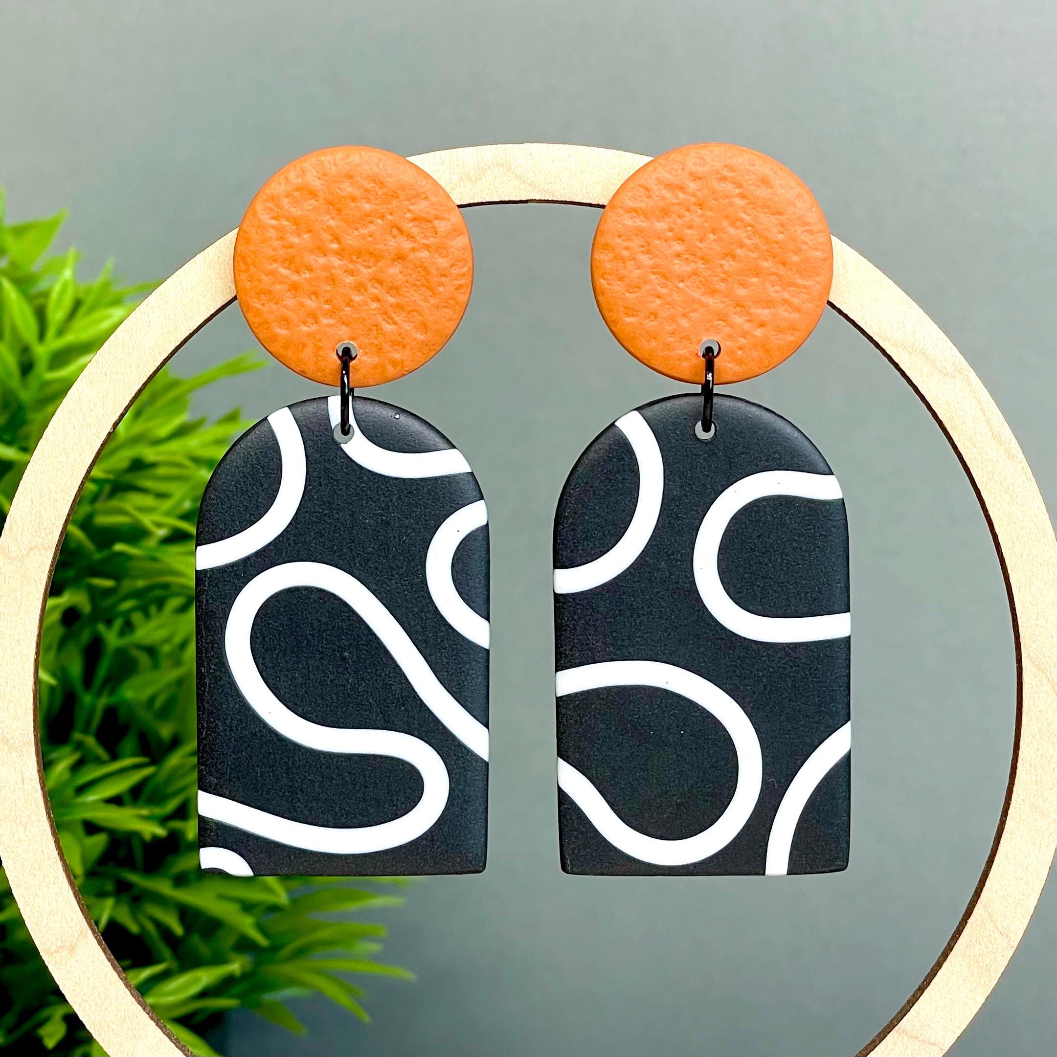 Pair of earrings with orange tops and black and white squiggle patterned bottoms
