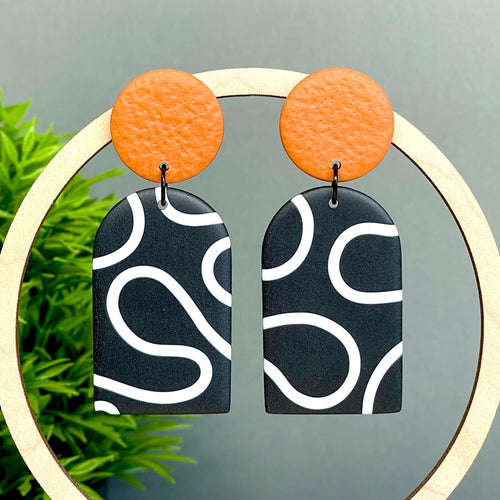 Pair of earrings with orange tops and black and white squiggle patterned bottoms