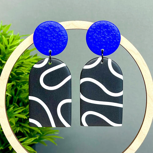 Earrings with electric blue tops and black and white squiggle patterned bottoms