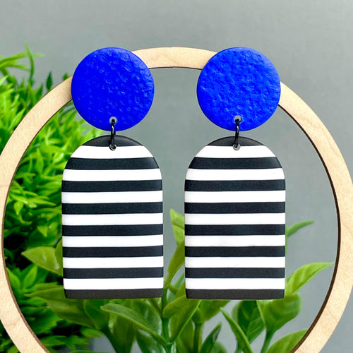 Pair of earrings with blue tops and black and white striped bottoms on a leafy background.