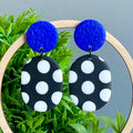 Black and white polka dot earrings with electric blue tops on a green plant background