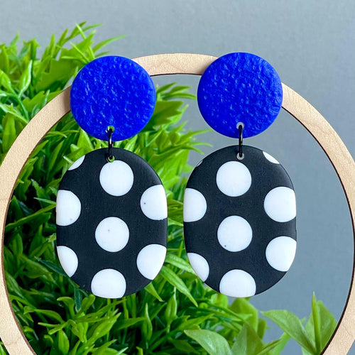 Black and white polka dot earrings with electric blue tops on a green plant background