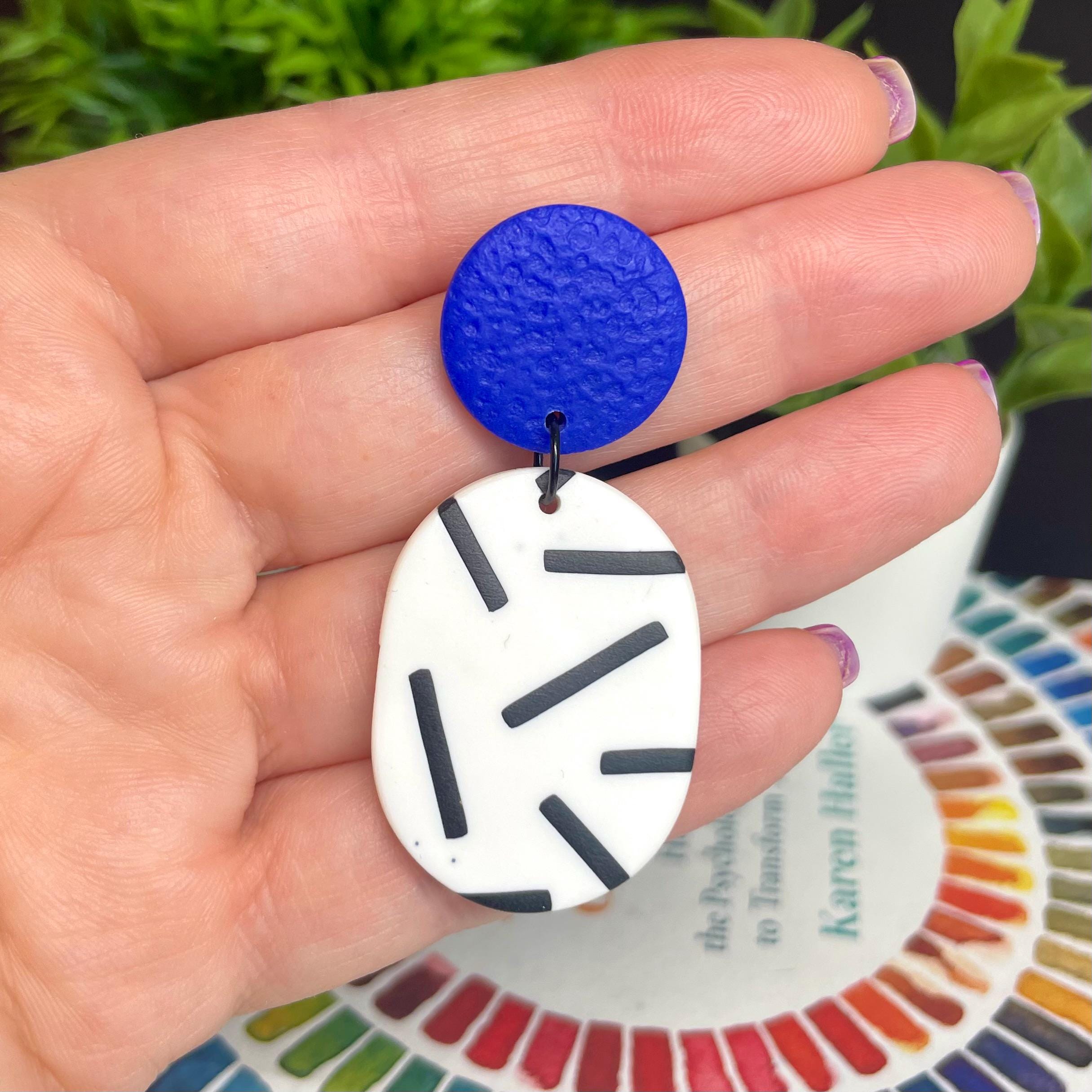 Hand holding electric blue top and mono sprinkle oval earrings against a colour wheel background