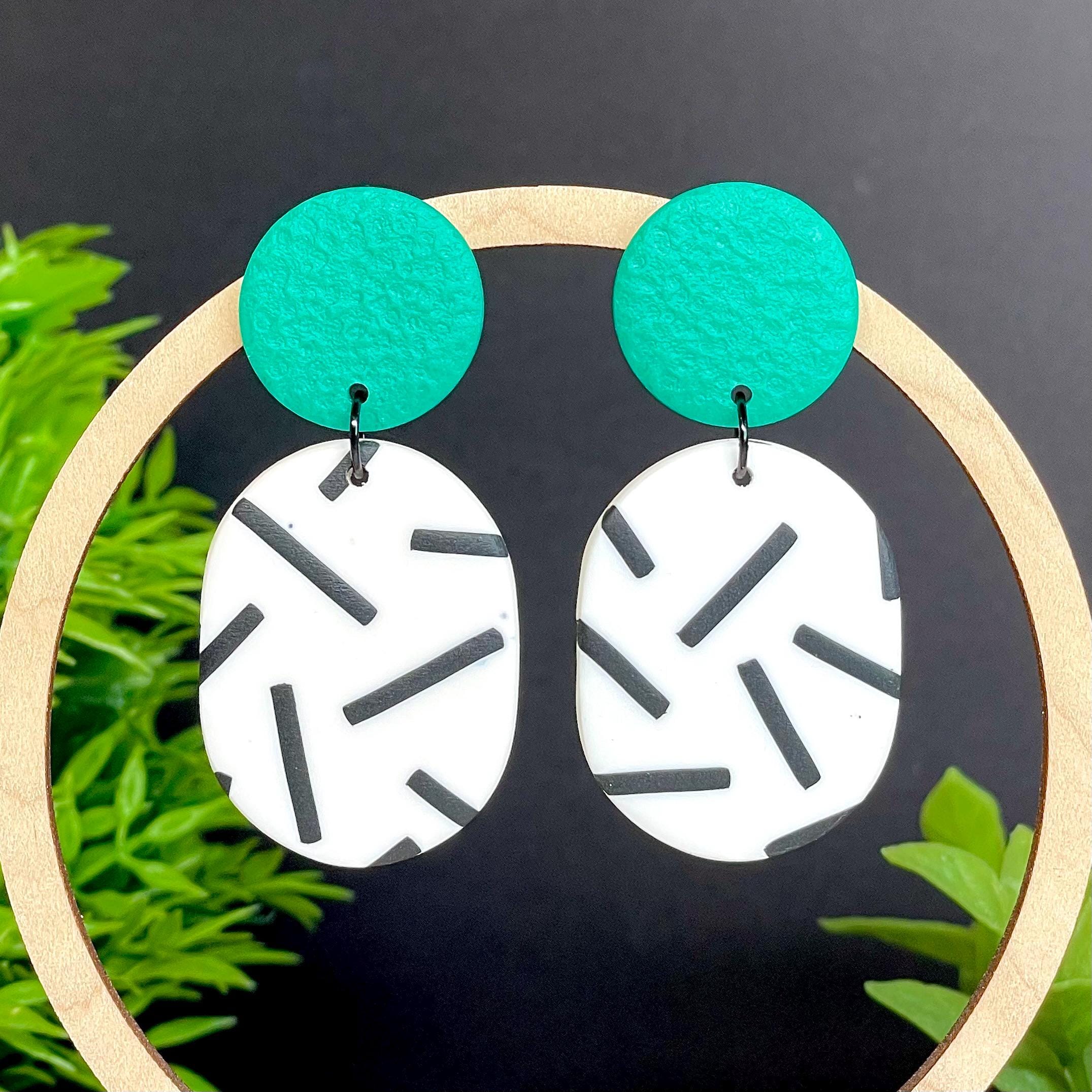 Earrings with emerald green tops & monochrome sprinkle oval bottoms, displayed on a wooden hoop against a dark background with greenery.