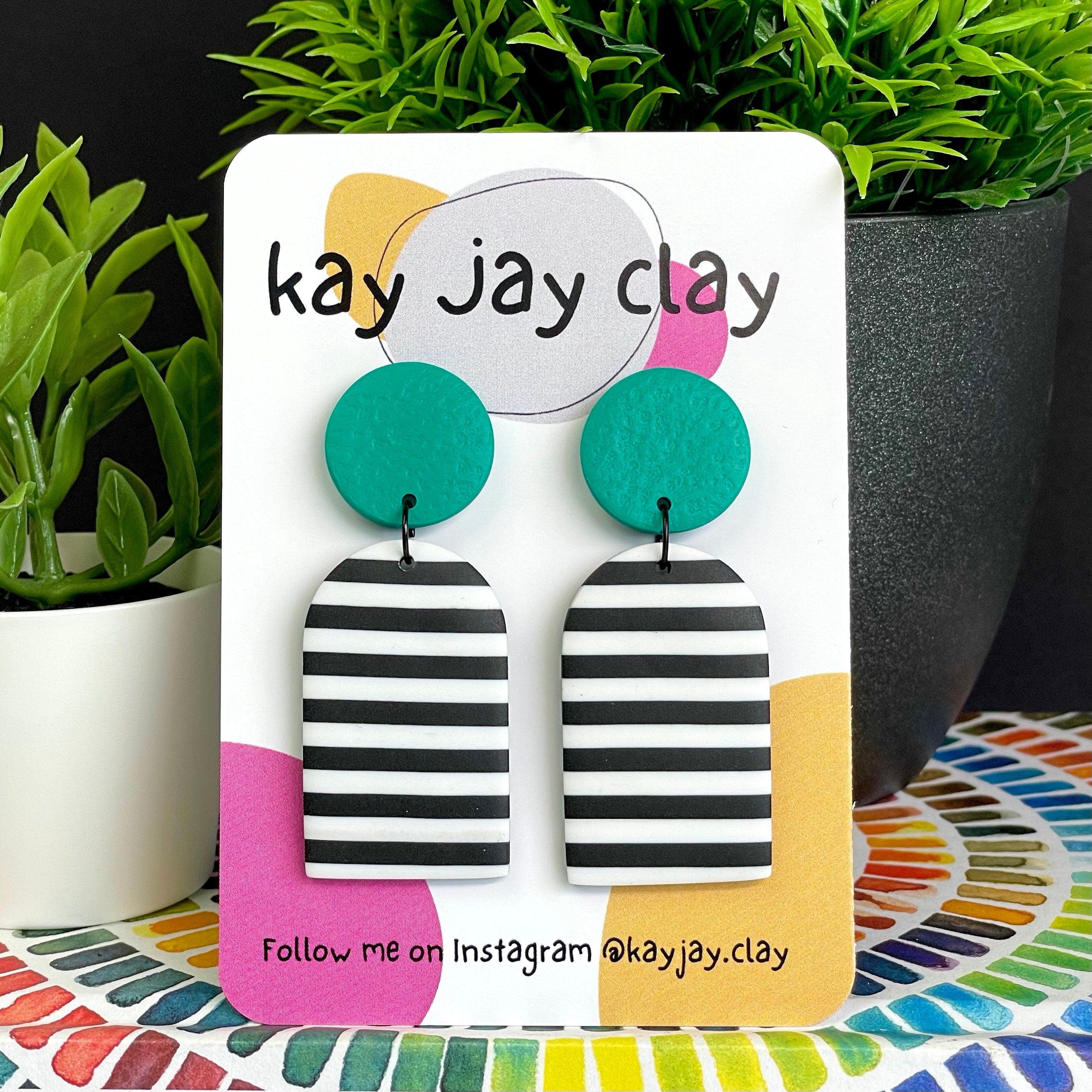 Green mono stripe dangle earrings on a 'kay jay clay' branded card with plants in the background