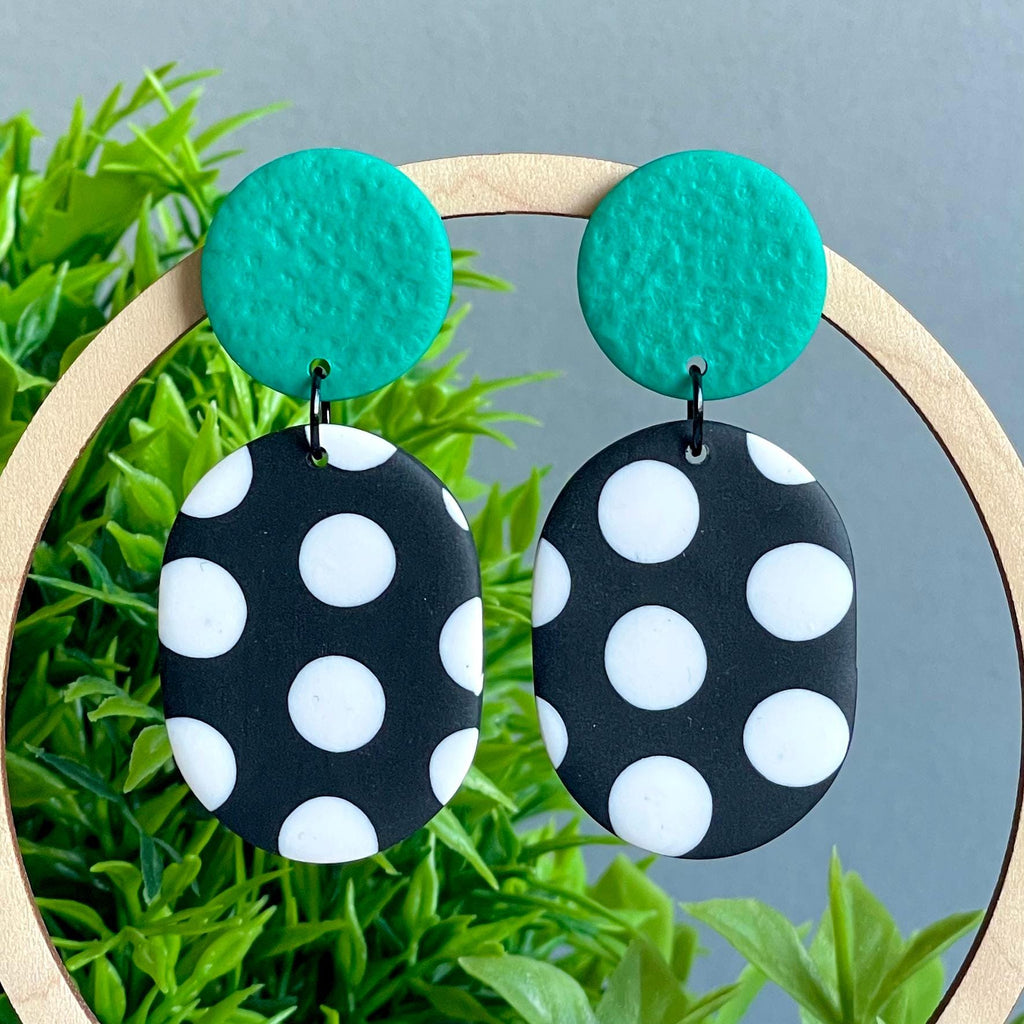 Black and white polka dot earrings with emerald green tops on a green plant background