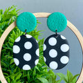 Black and white polka dot earrings with emerald green tops on a green plant background