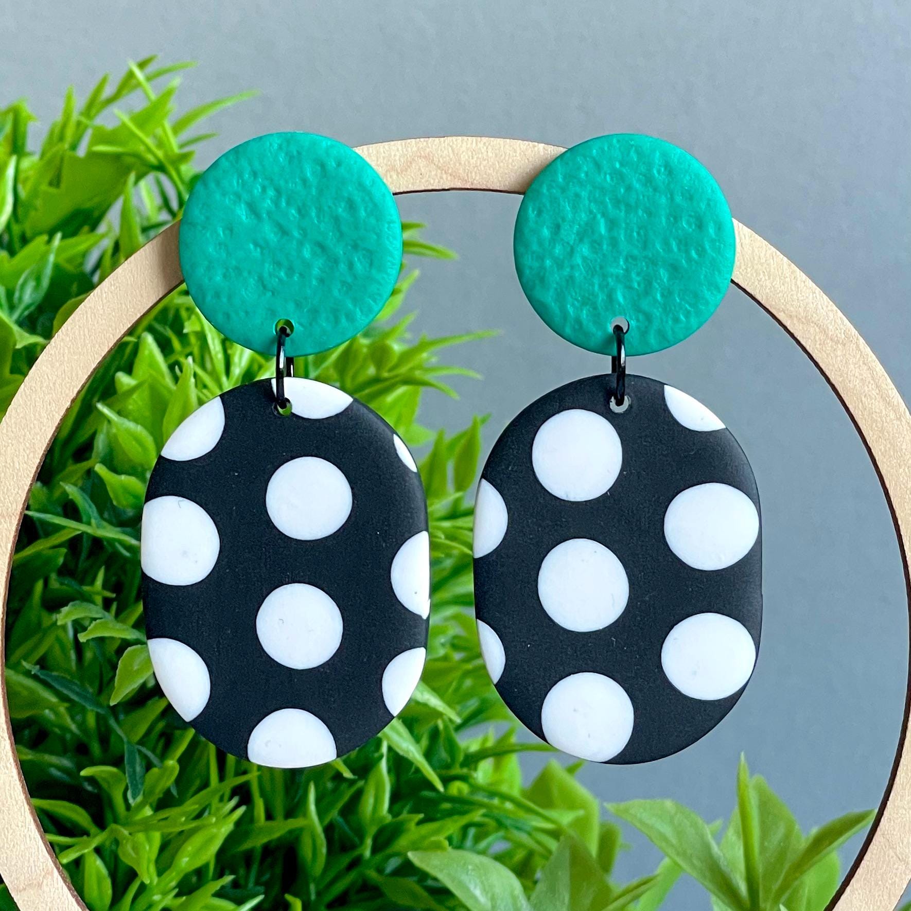 Black and white polka dot earrings with emerald green tops on a green plant background