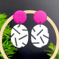Earrings with hot pink top & monochrome sprinkle oval bottom, displayed on a dark background with green leaves.