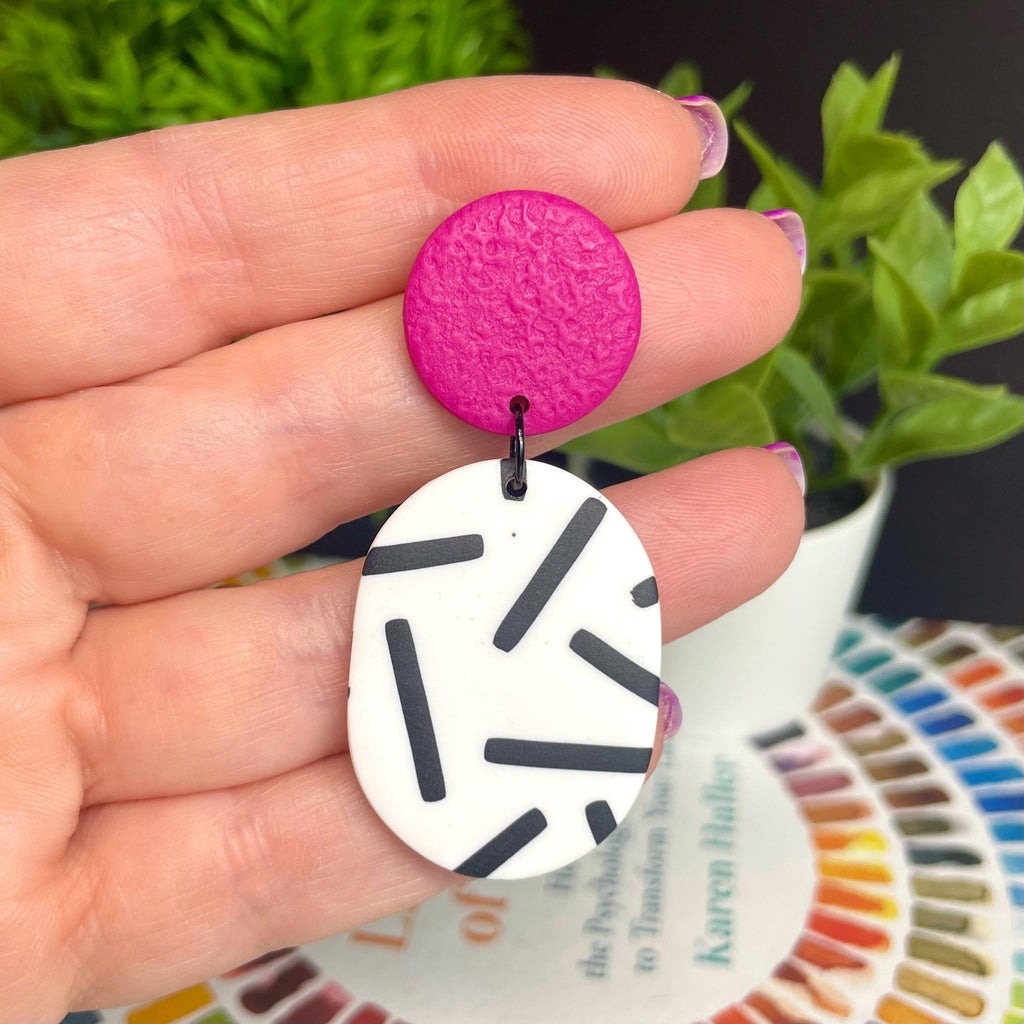 Hand holding an earring with hot pink top & monochrome sprinkle oval bottom against a bright background