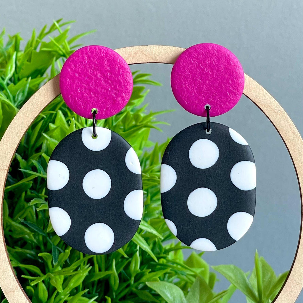 Earrings with pink tops and black and white polka dot bottoms on a grass background