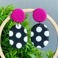 Earrings with pink tops and black and white polka dot bottoms on a grass background