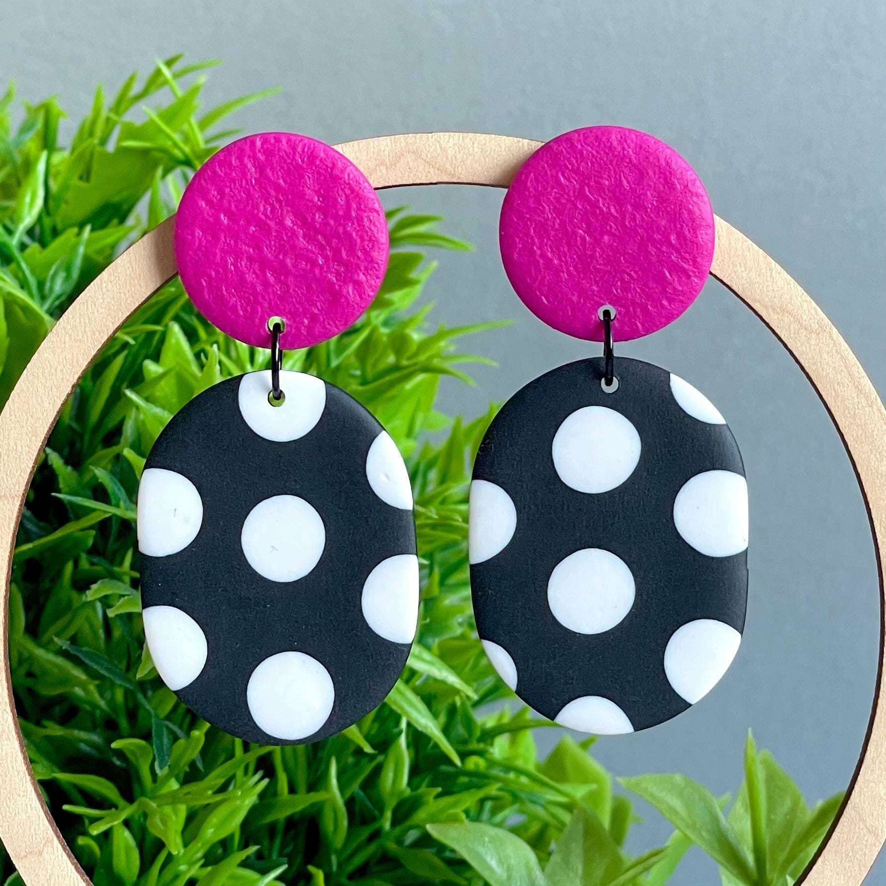 Earrings with pink tops and black and white polka dot bottoms on a grass background