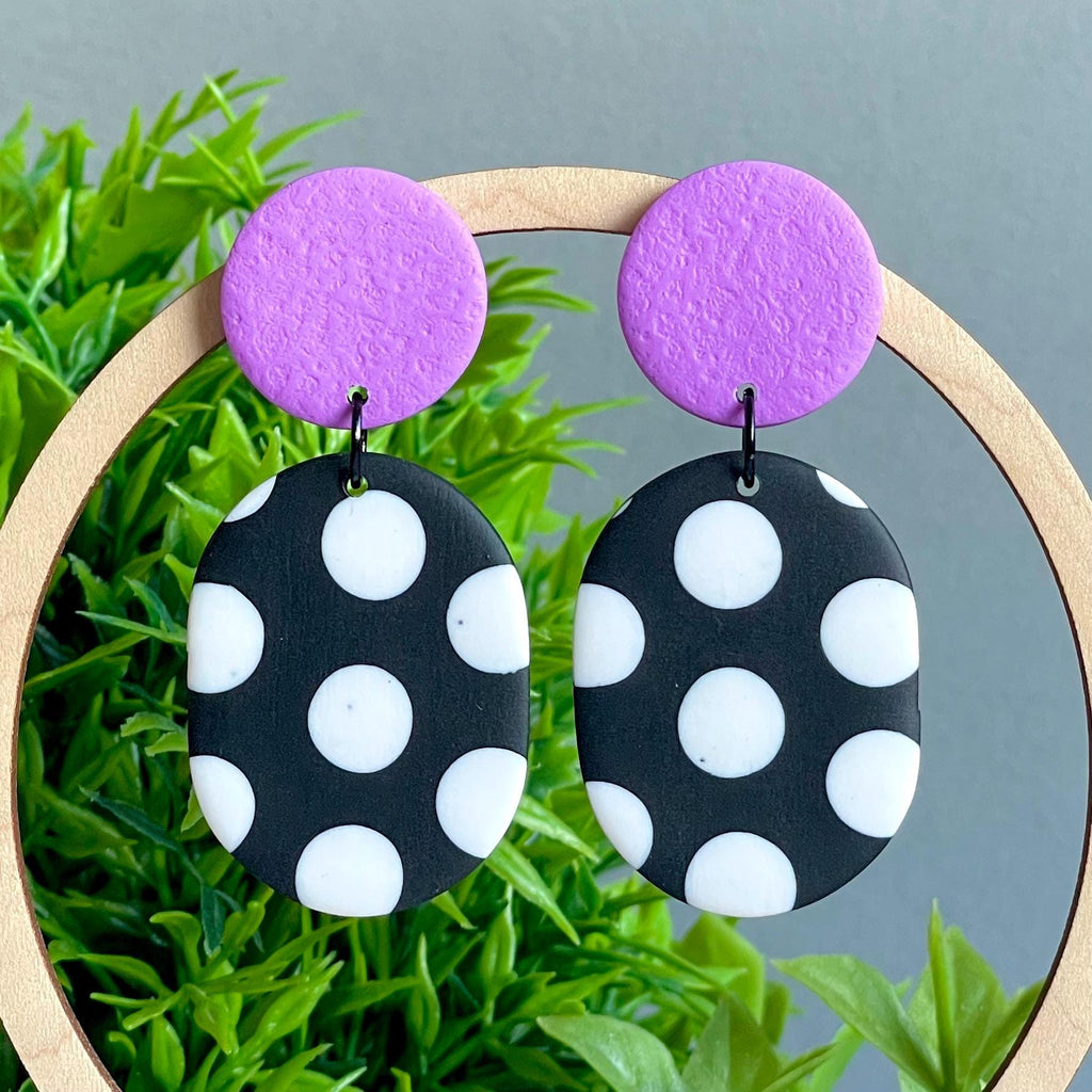 Black and white polka dot earrings with lilac purple tops on a green plant background
