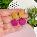 Mustard Yellow & Hot Pink colour pop dangle earrings held in hand for size reference