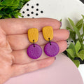 Mustard Yellow & Purple colour pop dangle earrings held in hand for size reference