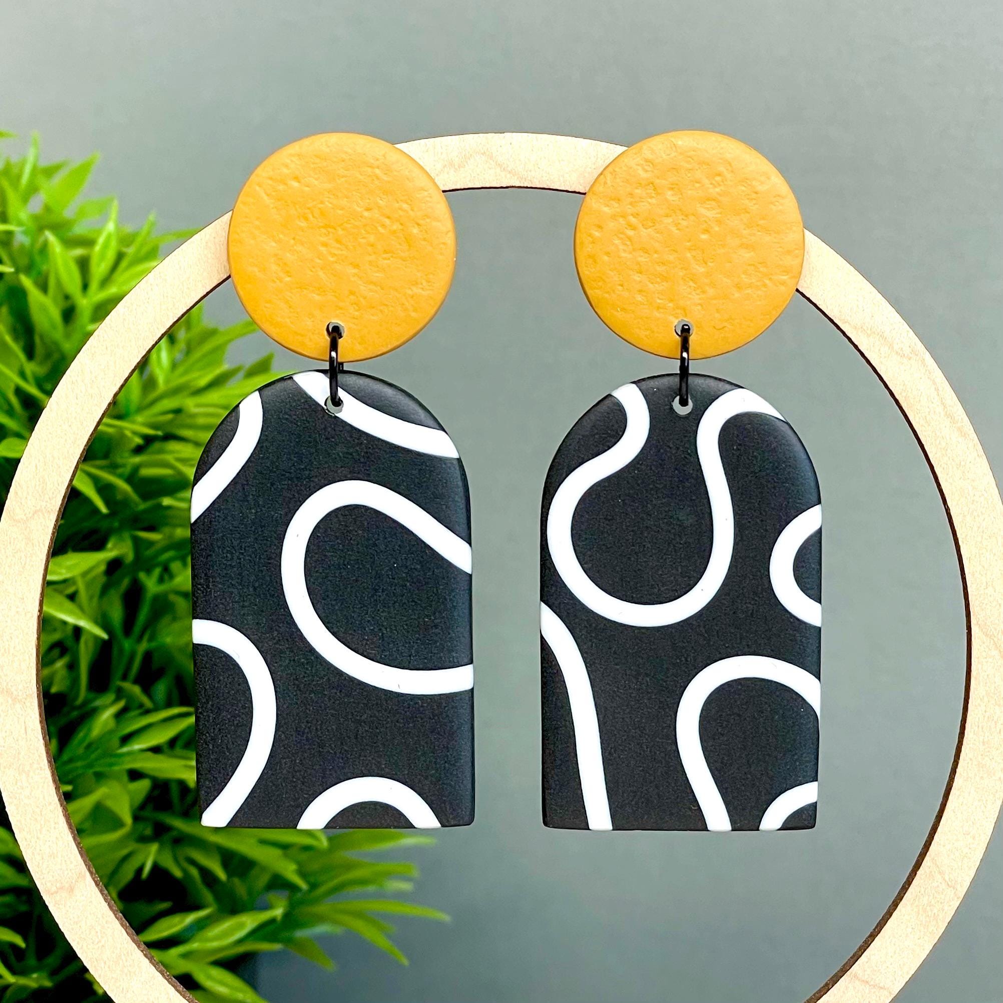 Pair of earrings with black and white squiggle patterned arch dangles and mustard yellow tops