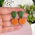 Olive Green & Orange colour pop dangle earrings held in hand for size reference