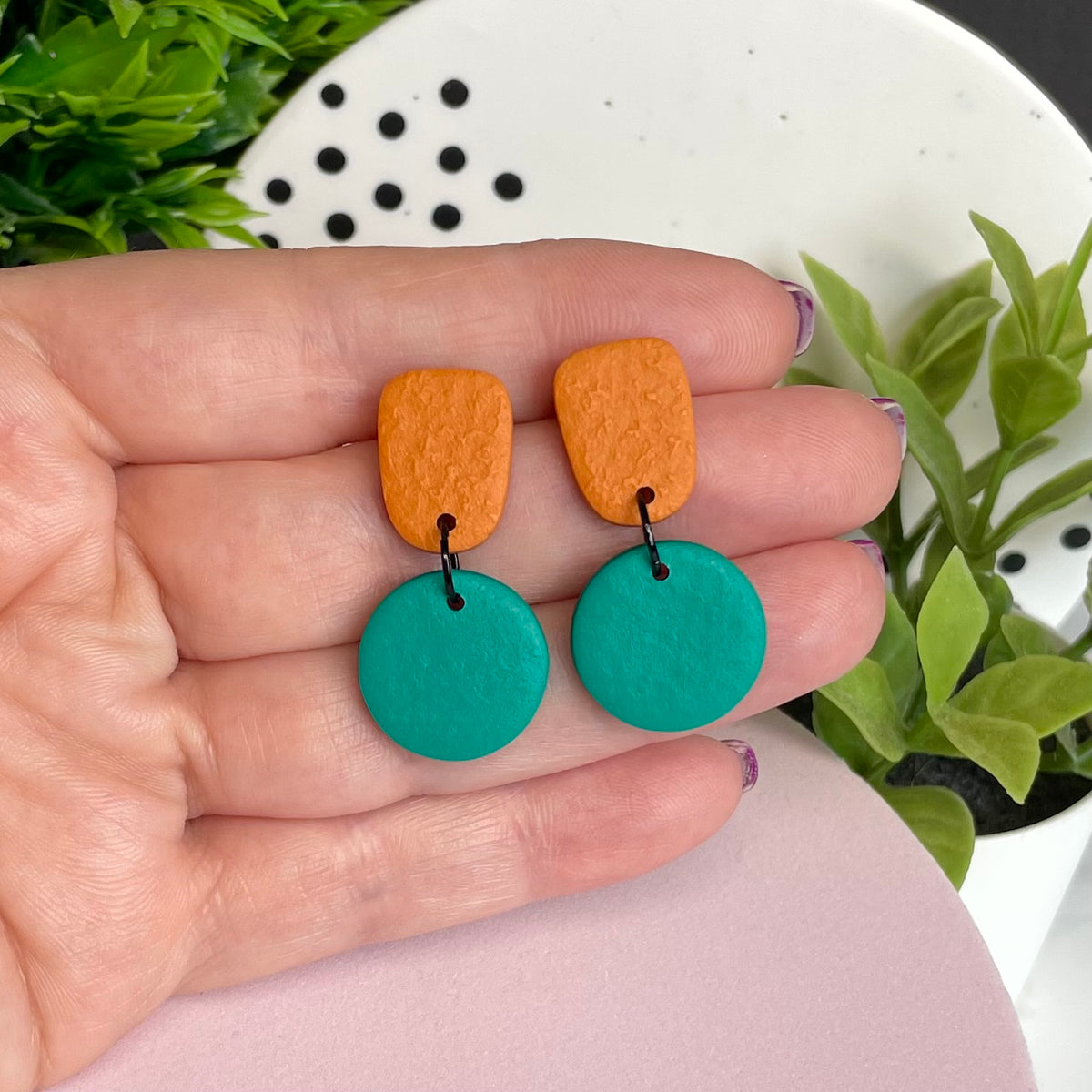 Orange & Emerald Green colour pop dangle earrings held in hand for size reference