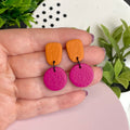 Orange & Hot Pink colour pop dangle earrings held in hand for size reference