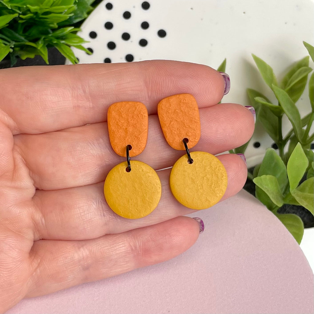 Orange & Mustard Yellow colour pop dangle earrings held in hand for size reference