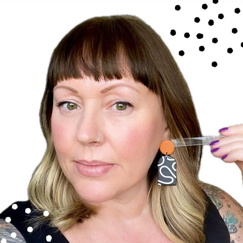 Try on picture of Kerry from Kay Jay Clay wearing the monochrome squiggle dangle earrings with a burnt orange top for size reference