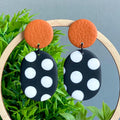Pair of earrings with orange circle top and black and white polka dot oval bottom