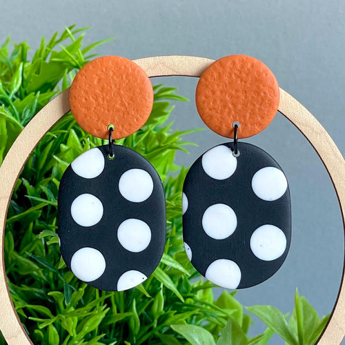 Pair of earrings with orange circle top and black and white polka dot oval bottom