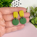 Pistachio & Olive Green colour pop dangle earrings held in hand for size reference