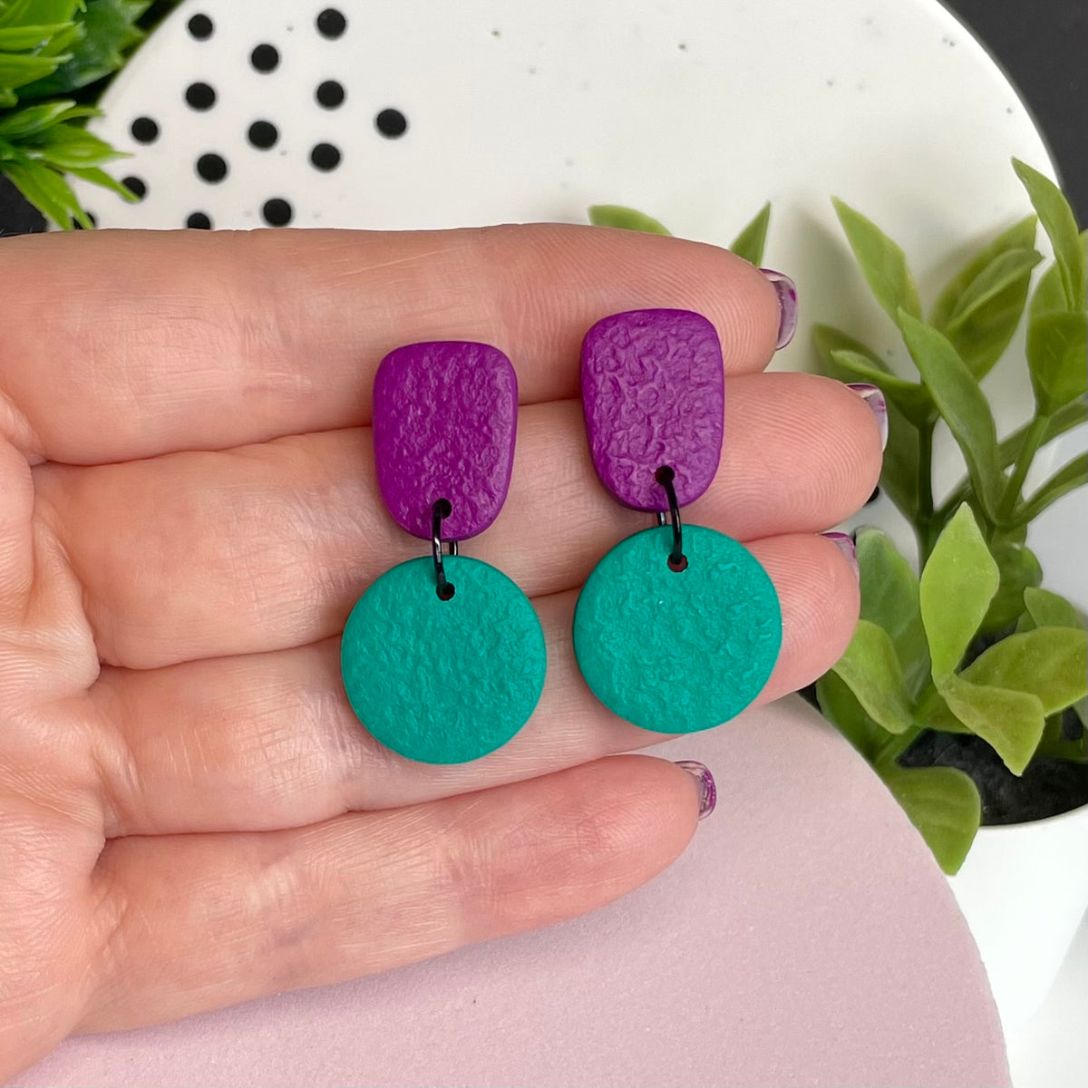 Purple & Emerald Green colour pop dangle earrings held in hand for size reference