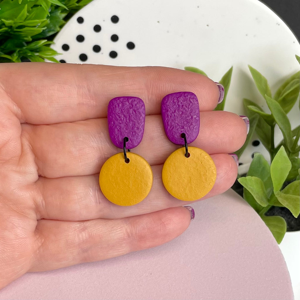 Purple & Mustard Yellow colour pop dangle earrings held in hand for size reference