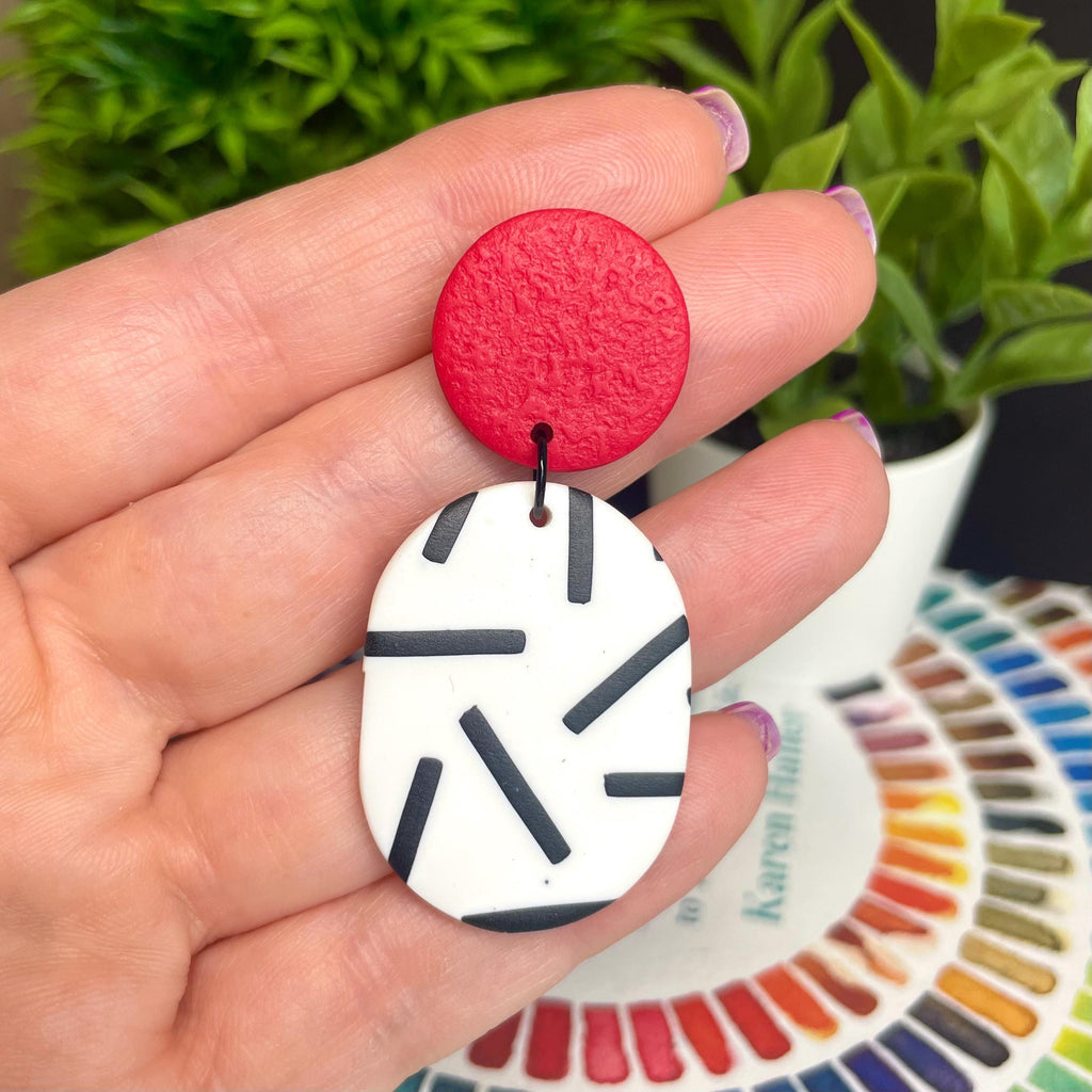 Red and white monochrome sprinkle earrings held by a hand with a colour swatch in the background