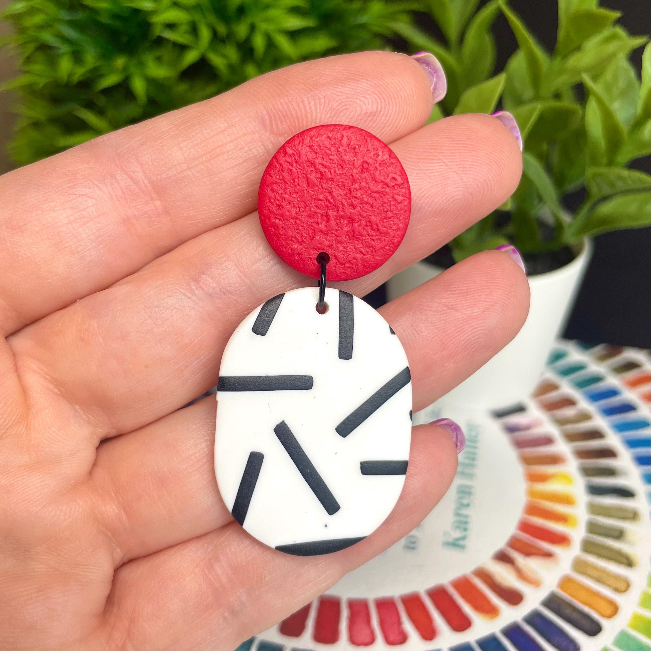 Red and white monochrome sprinkle earrings held by a hand with a colour swatch in the background