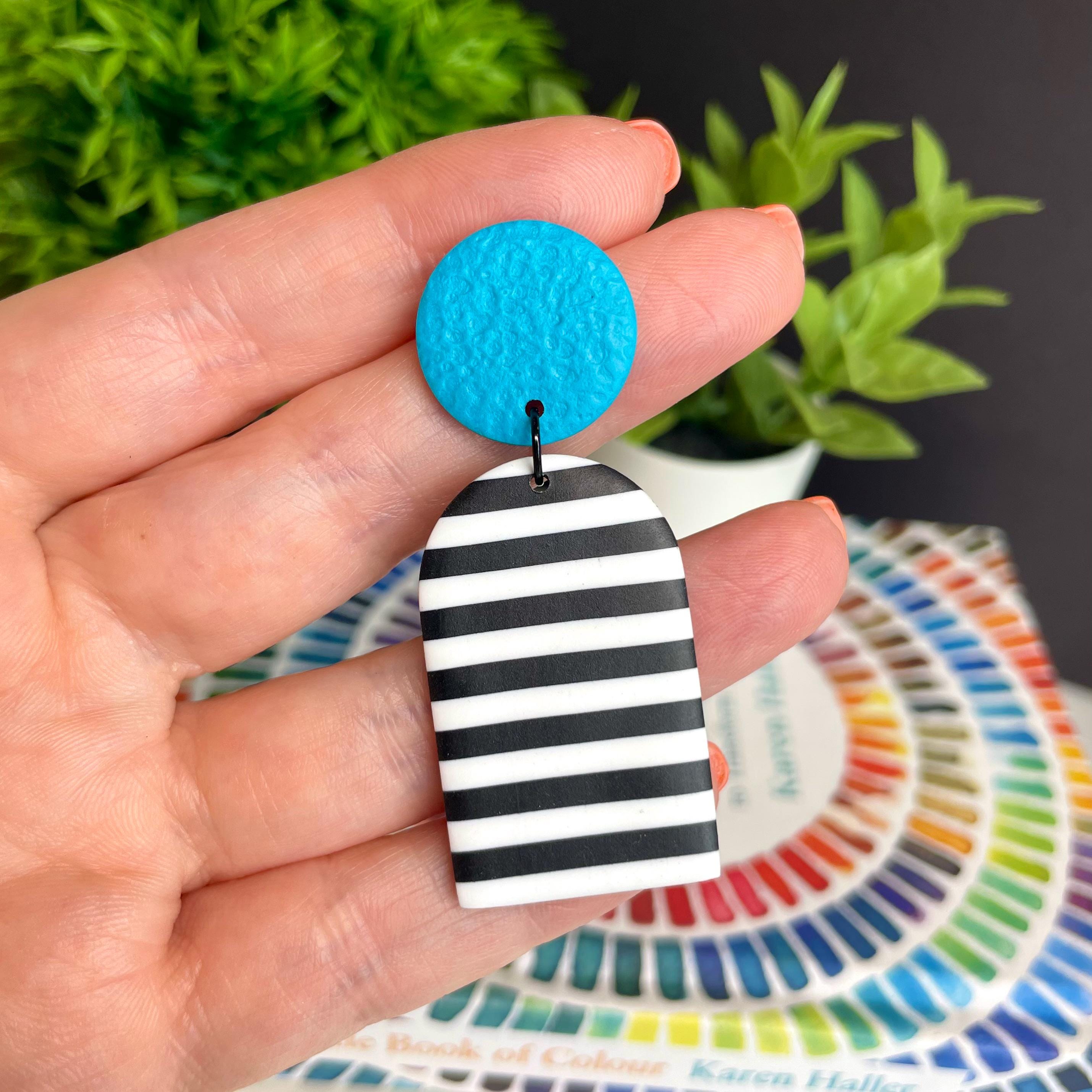 Earring with turquoise top and black and white striped bottom held in a hand