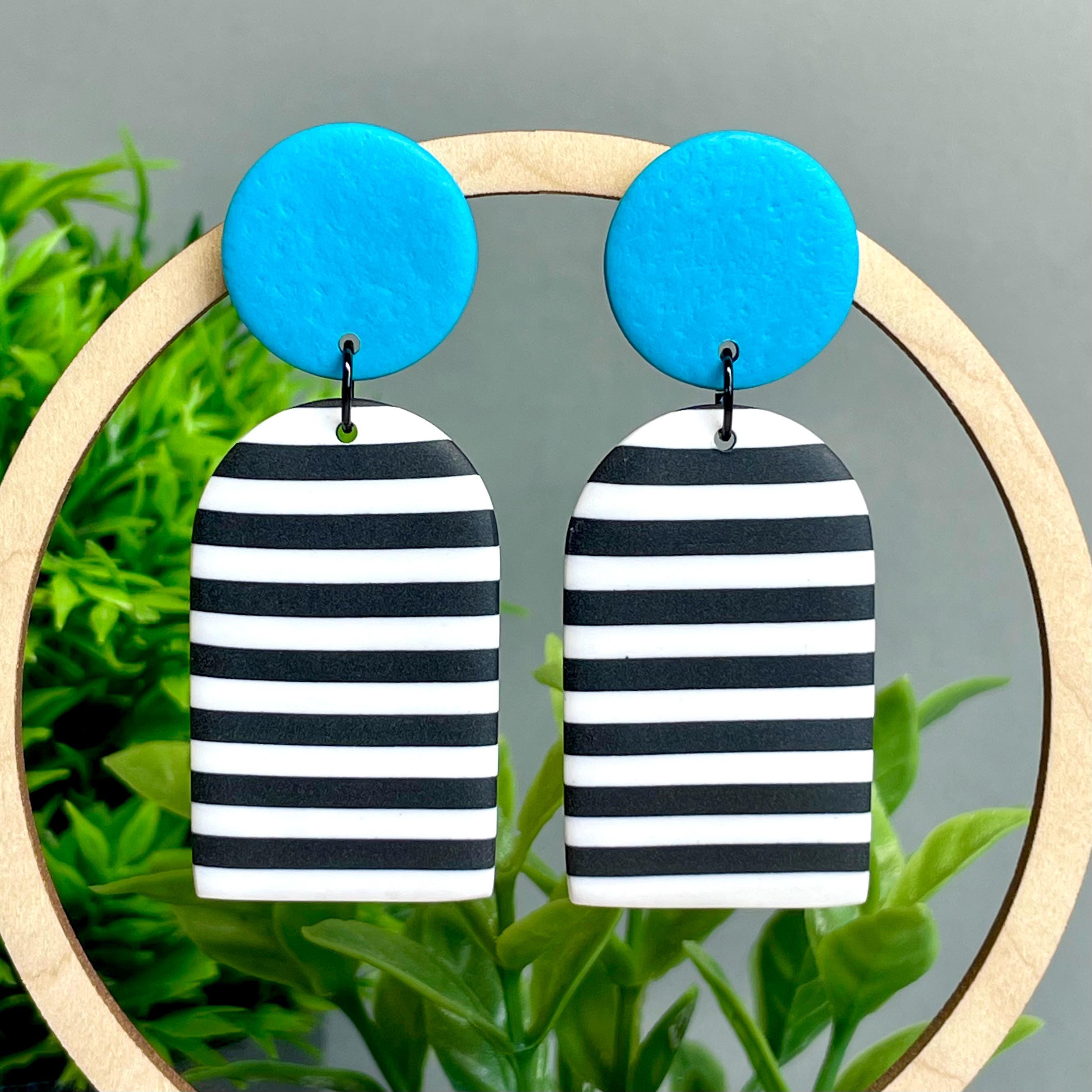 Black and white striped earrings with turquoise circular tops on a wooden stand against a natural background.