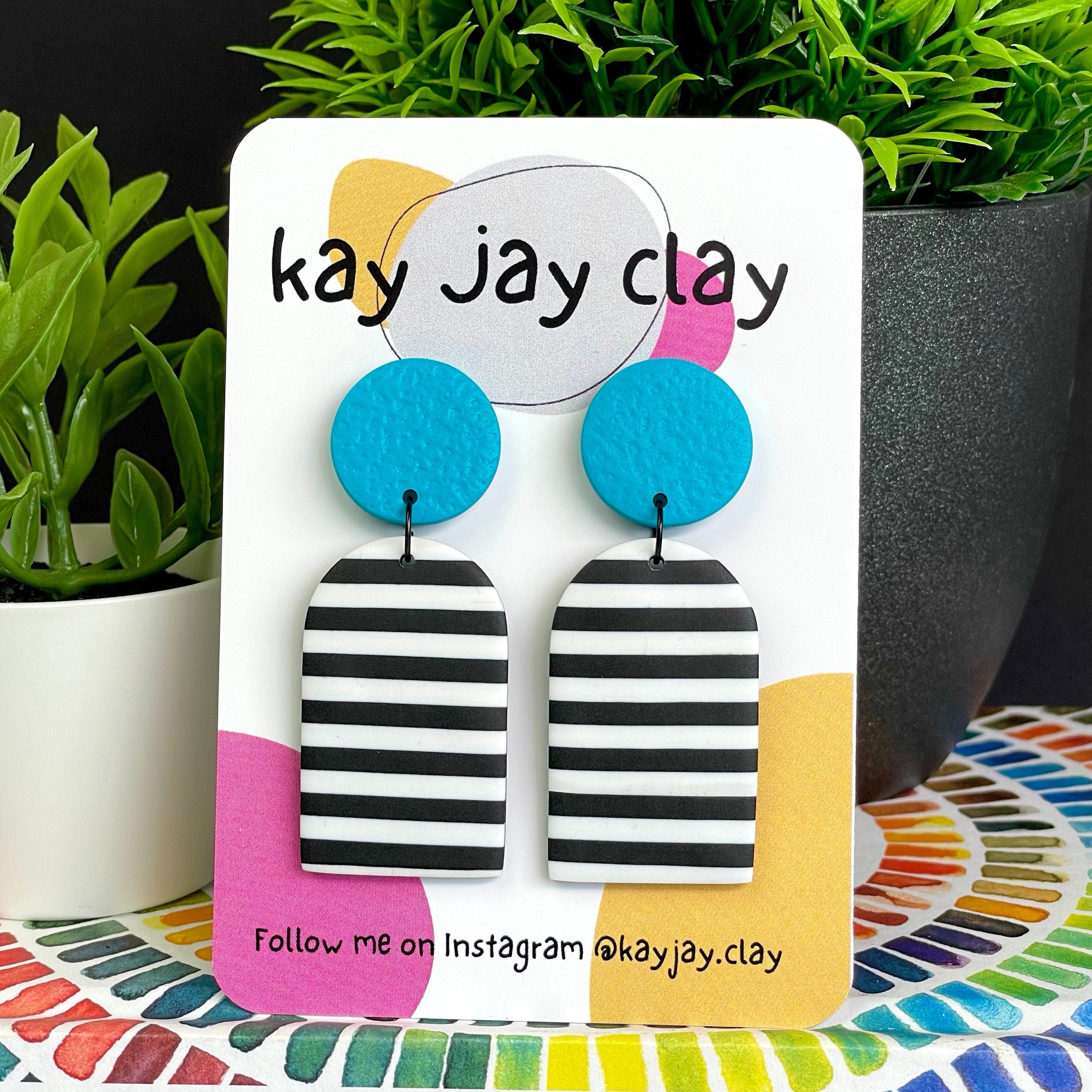 Turquoise mono stripe earrings on a 'kay jay clay' branded card with plants in the background