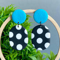 Earrings with turquoise top and black bottom with white polka dots on a green leaf background