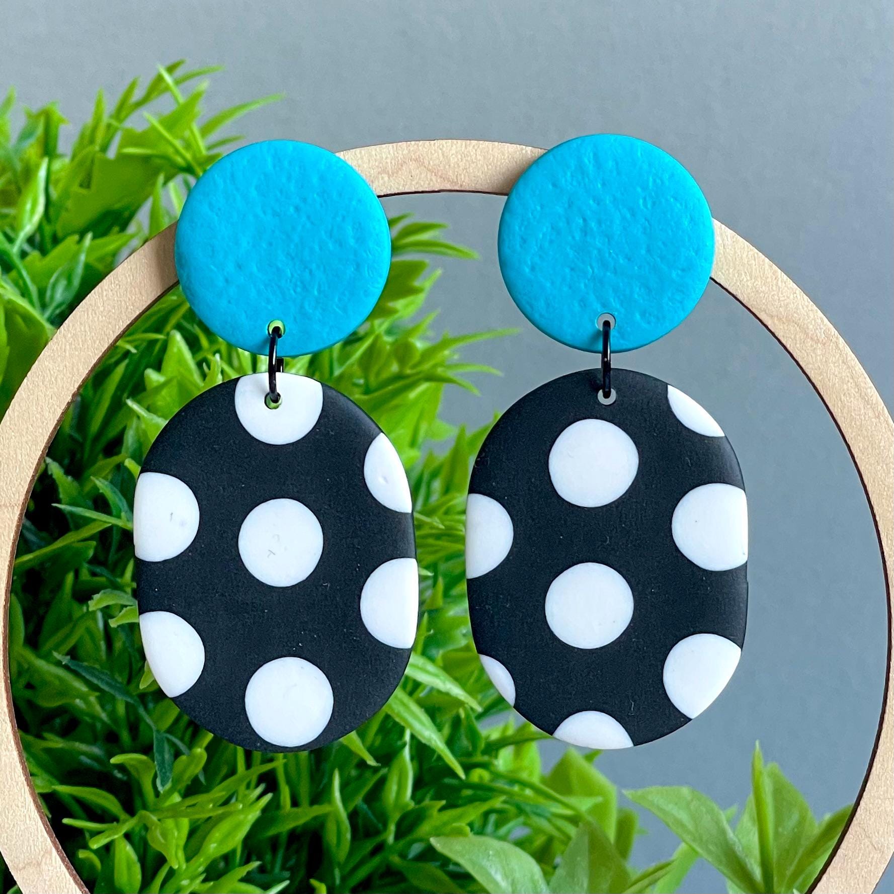 Earrings with turquoise top and black bottom with white polka dots on a green leaf background