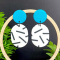 Earrings with turquoise tops and monochrome sprinkle oval bottoms, displayed on a dark background with greenery.