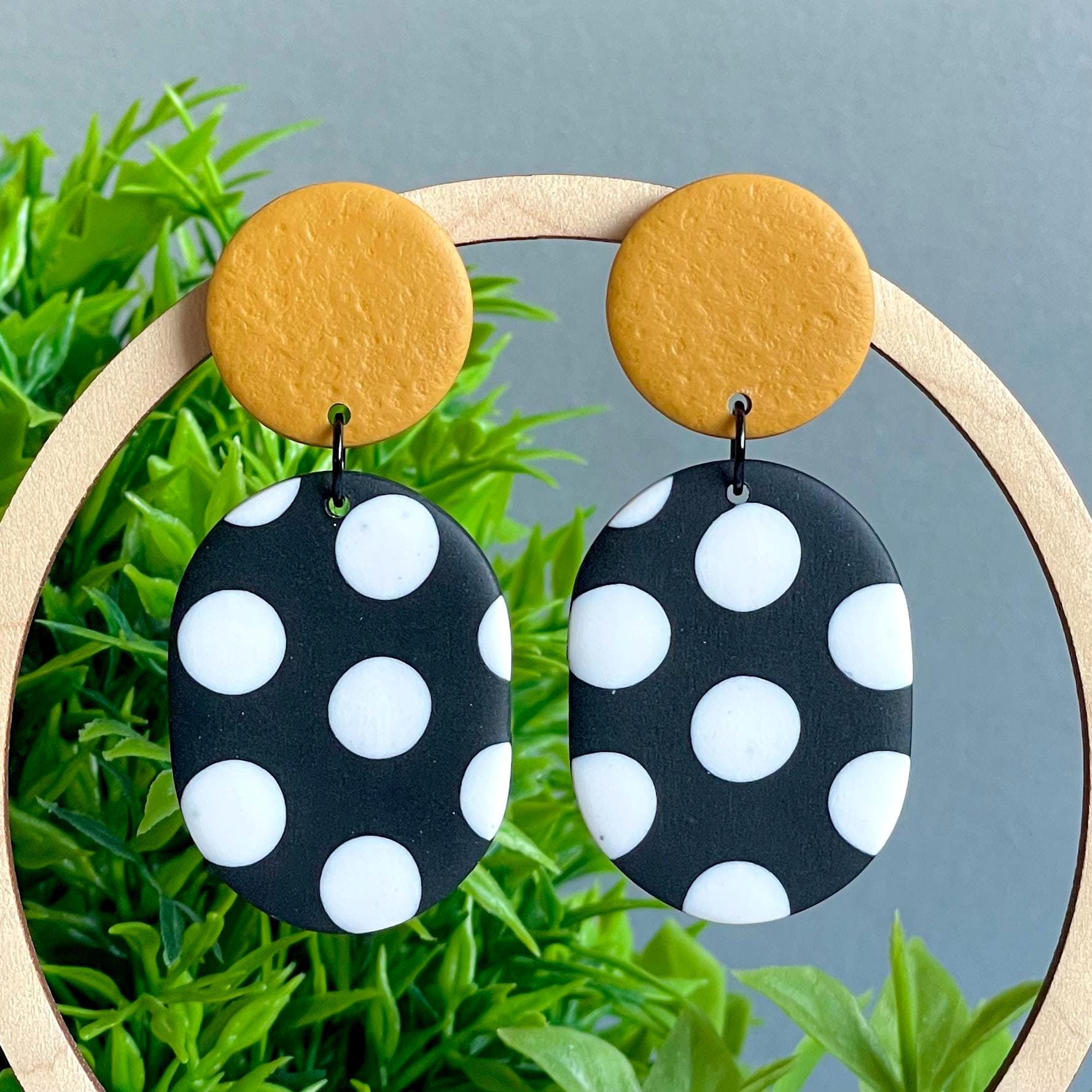 Black and white polka dot earrings with mustard yellow tops on a green plant background